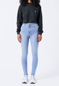 Czarna krótka bluza z małym logo, zestawiona z jasnoniebieskimi, wysokim stanem i wąskimi dżinsami oraz białymi trampkami. Widoczne szczegóły faktury tkaniny.