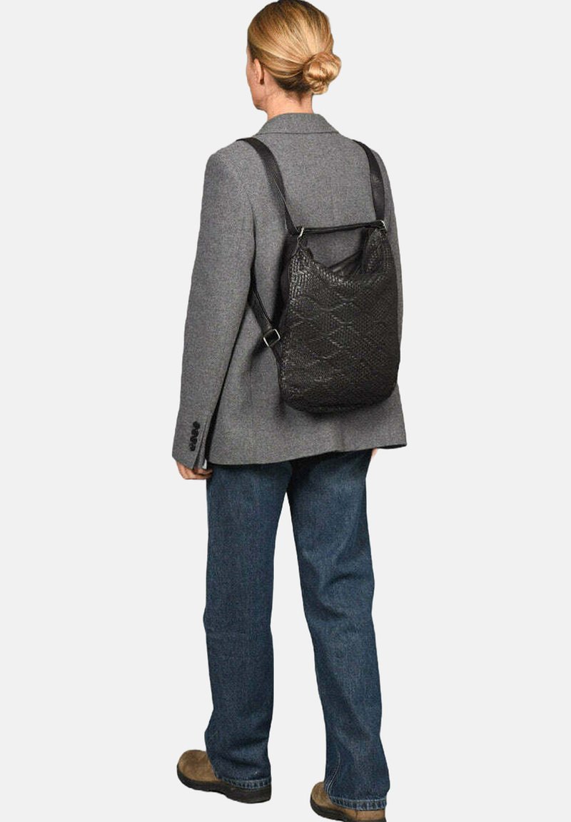Zwarte gestructureerde rugzak met een patroon, voorzien van verstelbare schouderbanden en in driehoekige vorm, gedragen over een grijze blazer.