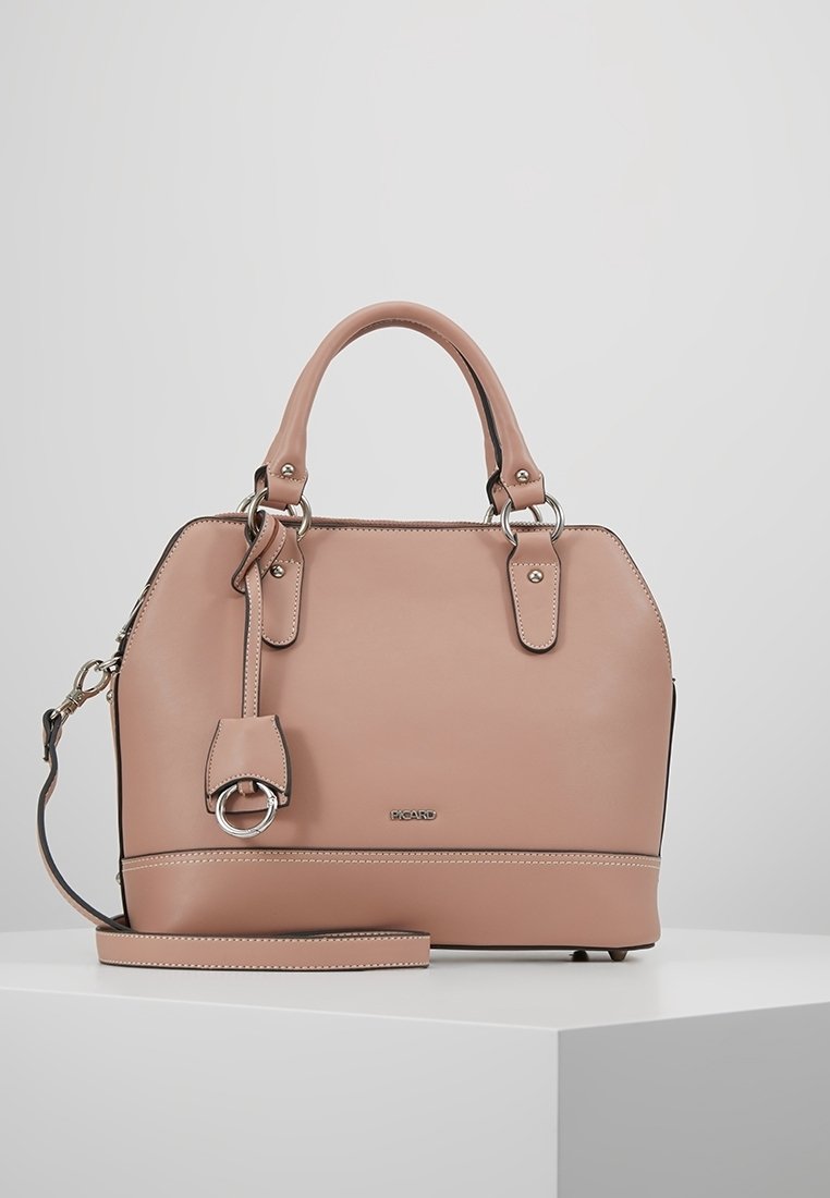 Sac à main en cuir rose blush avec doubles poignées, bandoulière amovible, anneaux argentés et petite plaque logo sur le devant, posé sur une surface blanche.
