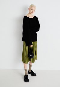 Black knitted sweater with oversized sleeves, paired with a pleated olive green skirt. Accessories include a dotted black bag and striped socks.