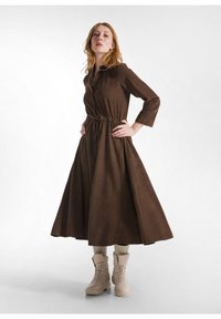 Vestito marrone, con bottoni, maniche lunghe e vita arricciata. Design a linea, realizzato in tessuto morbido, abbinato a stivali beige con lacci e calze color crema.