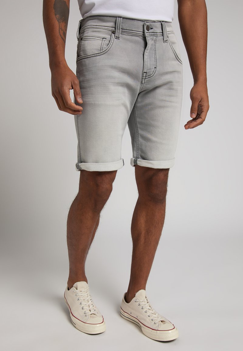 Shorts de mezclilla gris con un corte ajustado, dobladillos enrollados, cinco bolsillos y costuras en contraste, combinados con zapatillas de color claro.