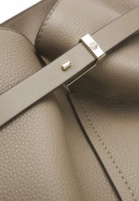 Sac à main en cuir beige texturé avec une sangle en cuir assortie, doté d'une petite boucle dorée et d'un logo embossé sur la quincaillerie.