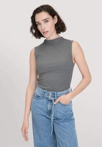 Graues ärmelloses Ribbed-Tanktop mit hohem Kragen, kombiniert mit hoch taillierten hellblauen Jeans aus Denim mit einem Bindegürtel und leichten Used-Effekten.
