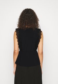 Černý bezrukávový top s krajkovými detaily na ramenech, kulatým výstřihem, peplum pasem a volným střihem. Zadní pohled ukazuje složité krajkové akcenty.