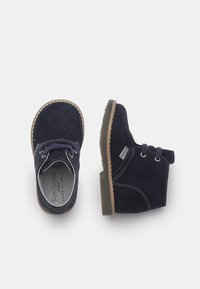 Navyblaue Wildlederschuhe für Kleinkinder mit beiger Naht und Schnürsenkeln, einer von oben und der andere von der Seite gezeigt, auf einem weißen Hintergrund.