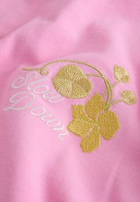 Lyserødt stof med guld- og hvid broderi. Har teksten "Slow Down" og blomsterdesigns i en tekstureret sting.