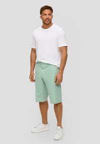 Shorts verts clairs en coton, avec un design à l'avant plat et des poches latérales, associés à un tee-shirt blanc uni et des baskets blanches.