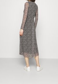 Robe à manches longues en tissu noir transparent, avec une silhouette fluide, une taille cintrée et des baskets blanches comme chaussures.