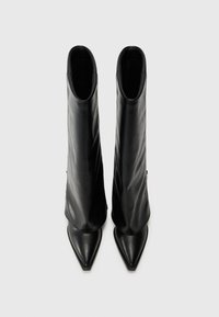 Bottes en cuir noir montantes avec un design élégant, bouts pointus et texture lisse, présentant une silhouette ajustée et un matériel minimal.
