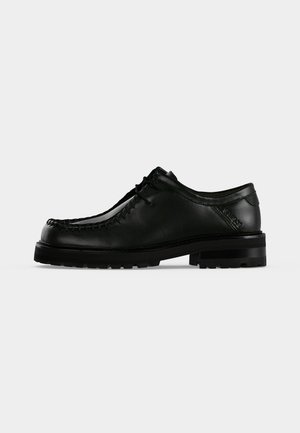 Chaussure en cuir noir à lacets avec semelle épaisse en caoutchouc et couture moc toe, vue de profil gauche sur fond clair uni.