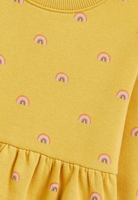 Vestido amarillo con un tejido texturizado, que presenta pequeños patrones de arcoíris bordados. El detalle del dobladillo con volantes añade una apariencia de capas.