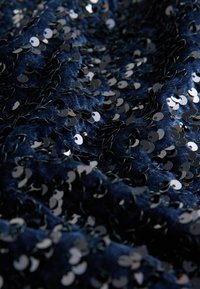 Navy blue fabric covered in reflective silver sequins, creating a textured surface with circular patterns and a shimmering effect.