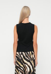 Black sleeveless top with a round neckline, featuring a gathered waist detail. Paired with a patterned skirt in beige and black stripes.