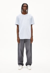 Lichtblauwe katoenen t-shirt met een ronde hals en korte mouwen, met een subtiele geborduurde afbeelding; grijze wijde spijkerbroek en witte sneakers.