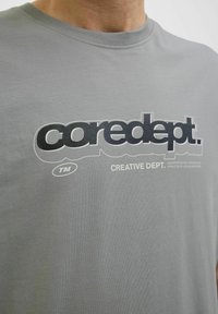Grå bomulds t-shirt med et stort sort grafisk tryk, der viser teksten "coredept." og "CREATIVE DEPT.". Klassisk crew neck design.