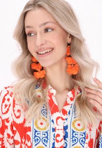 Bluză cu un model alb și roșu, având accente albastre și galbene, și cercei florali strălucitori în nuanța portocalie; textură fină și design detaliat.