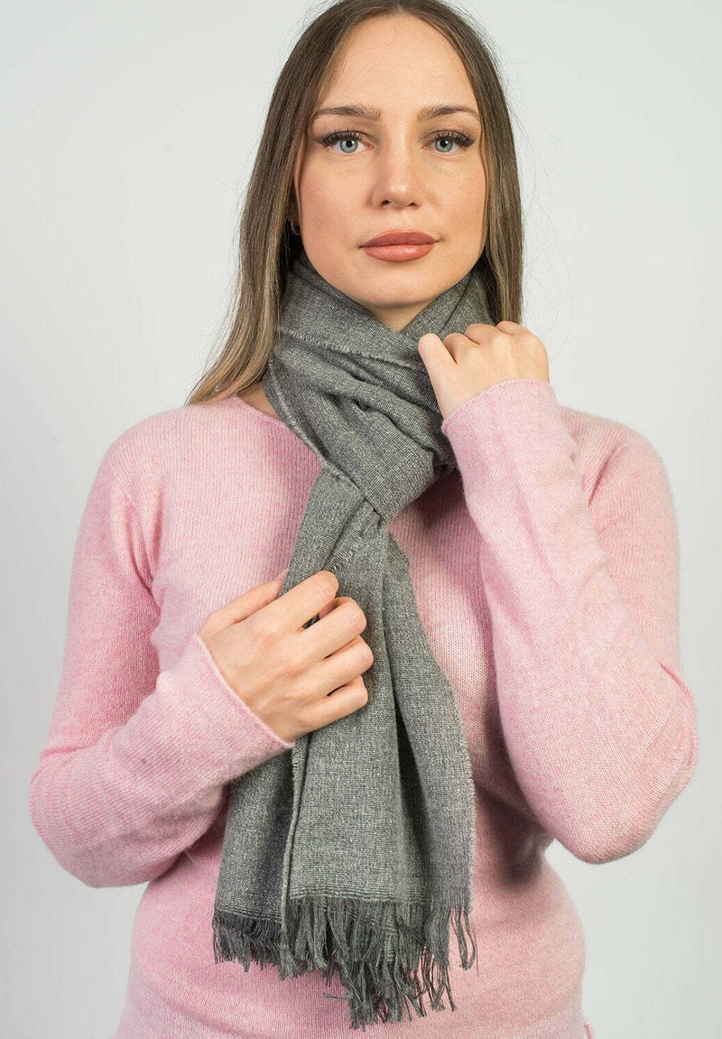 Grå scarf i mjukt material med fransiga ändar. Buren runt halsen med en ljusrosa tröja synlig under.