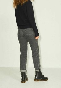 Maglione lavorato a maglia nero, jeans grigi dal taglio affusolato e stivali neri con lacci e suola spessa. I jeans hanno i risvolti e tasche posteriori.