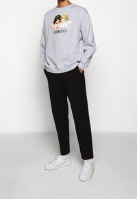 Sudadera gris con ángeles impresos y texto "FIORUCCI". Combinada con pantalones negros y zapatillas blancas; cuenta con un corte relajado y puños acanalados.