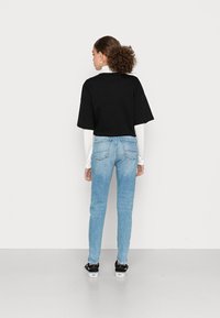T-shirt preto cropped por cima de uma blusa de mangas longas branca, combinada com jeans skinny azul claro e sapatilhas pretas com solas brancas.