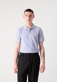 Hellblaues Polohemd mit ribbeltem Kragen und weißen Akzenten, mit kleinem CK-Logo. Tragen Sie dazu schwarze Hosen mit elastischem Bund.