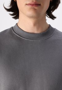 Felpa grigia con collo a giro, caratterizzata da un neckline a costine e una texture liscia, senza loghi o motivi visibili. Vista ravvicinata.