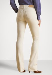 Jeans bege flare com textura suave e design de cinco bolsos, combinados com uma camisa azul-marinho às riscas e saltos apontados castanhos.