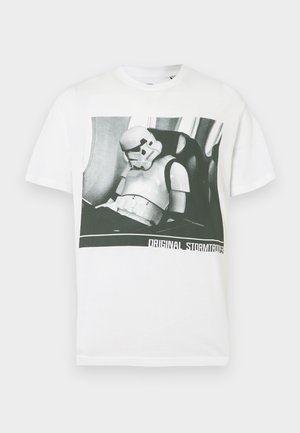 T-shirt bianca in cotone con grafica in bianco e nero di uno Stormtrooper. Sotto, il testo recita "ORIGINAL STORMTROOPER." Maniche corte e collo rotondo.