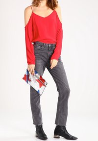 Rød off-the-shoulder bluse, grå lige jeans med frynser i kanten, sorte ankelstøvler og en multicolor clutch-taske med stjerne-accenter.