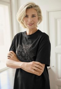 Melna kokvilnas T-krekls ar apaļu kakla izgriezumu, priekšpusē dekorēts ar metāla nagliņu ornamentu apaļās formās.