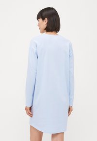 Ljusblå, långärmad T-shirtklänning gjord av mjukt tyg; har en rund halsringning och en avslappnad passform. Kanten är något rundad.