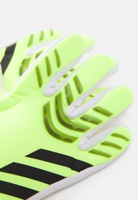 Neongula handskar med svarta detaljer och mönstrat grepp, tillverkade av texturerat material för förbättrat grepp och flexibilitet.