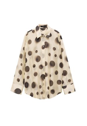 Blouse et jupe beige à gros et petits pois noirs, blouse partiellement déboutonnée, portée par une personne du cou à la taille.