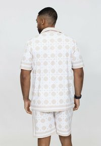 Ensemble comprenant une chemise à manches courtes et un short en beige clair avec un motif géométrique. Fabriqué en tissu doux, il présente un col évasé et des finitions contrastantes.