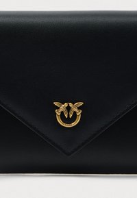 Fekete bőr boríték clutch, arany gyűrűs hardverrel, két madár díszítéssel, sima textúrával és éles háromszög alakú fedéllel.