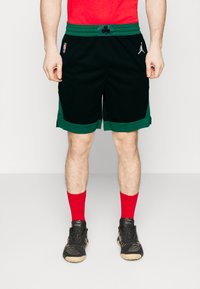 Sorte sports-shorts med grønne accenter og symboler, der har en elastisk talje. Parret med røde sokker og sorte sneakers.