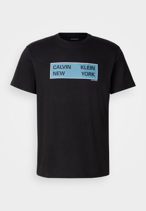 T-shirt de algodão preto com texto ousado em azul e preto: "CALVIN NEW KLEIN YORK" na frente. Design clássico de gola redonda, mangas curtas.
