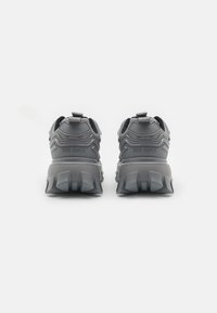 Gray athletic shoes with a textured upper, pronounced lugs on the outsole, and rear pull tabs; branding visible on the heel area.