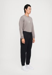 Szary długoszlfowy sweatshirt z logo, zestawiony z czarnymi joggerami o zwężanym kroju i białymi trampkami. Prosty design, miękka faktura i luźny krój.
