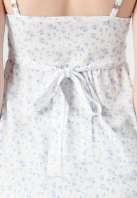 White fabric dress featuring small blue floral patterns, adjustable spaghetti straps, and a tied waist detail.
