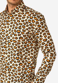 Camicia con stampa leopardata con sfondo crema, macchie nere e arancioni, colletto con bottoni e maniche lunghe aderenti. Tessuto liscio.