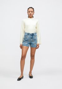 Suéter beige claro de manga larga, combinado con pantalones cortos de mezclilla azul con bordado floral y cintura alta. Bailarinas negras.