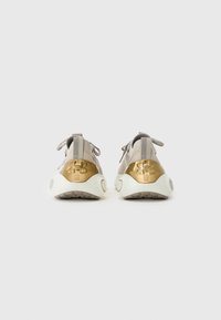 Sport shoes in light beige mesh with gold accents, textured back, rounded white sole, and laces for secure fit.