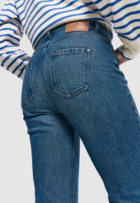Hochtaillierte blaue Jeans aus Denim mit einem verwaschenen Finish, zwei Gesäßtaschen und einem braunen Leder-Logo-Patch an der Taille.