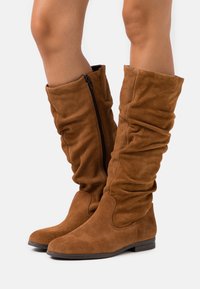 Bottes montantes en daim marron à la silhouette décontractée, dotées d'une fermeture éclair latérale et d'une semelle plate. Texture lisse avec des bouts arrondis.