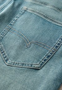 Poche de jean en denim bleu avec coutures doubles et surpiqûres décoratives en boucle au centre de la poche.