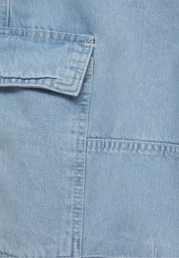 Tela de mezclilla azul claro con un bolsillo cosido, superficie texturada y líneas limpias con un sutil desgastado en ciertas áreas.
