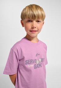 Hellviolettes Baumwoll-T-Shirt mit einem Grafikdruck von Volleyballs und dem Text "SERVE THE GAME" in Dunkelgrau, mit rundem Ausschnitt.