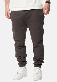 Dunkelgraue Jogginghosen aus weichem Material, mit elastischen Bündchen und lässiger Passform, kombiniert mit weißen Sneakern für einen Kontrast.